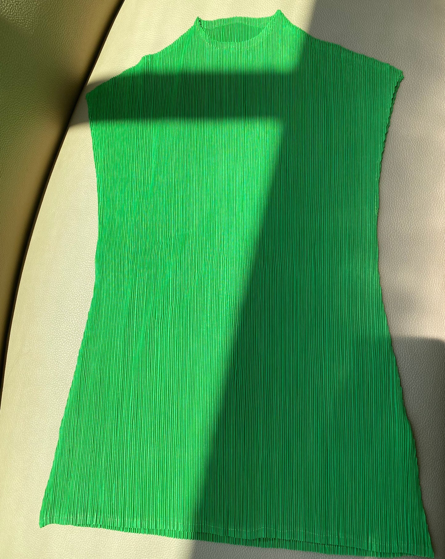 a green mock neck top in a kelly green tone lays flat on a tan couch with a sunbeam streaking across