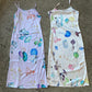 two slip dresses lay side by side on the concrete floor, one is lilac with a psychedlic mushroom print and the other has a pink base with a similar mushroom print