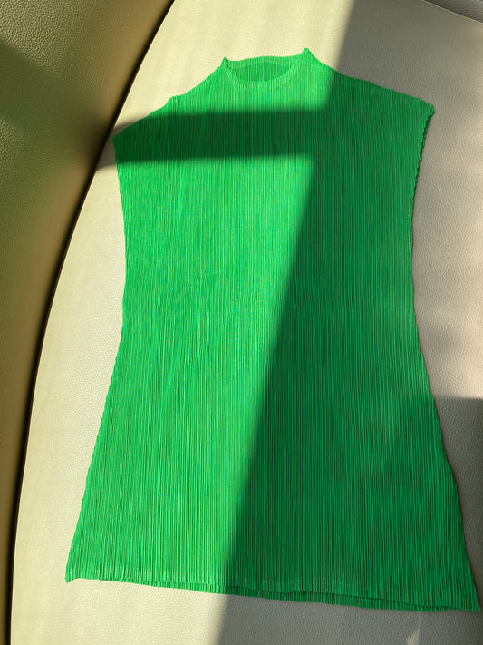 a green mock neck top in a kelly green tone lays flat on a tan couch with a sunbeam streaking across